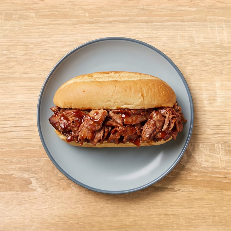 A pulled pork sandwich with barbecue sauce on a light blue plate, on a wooden table.
