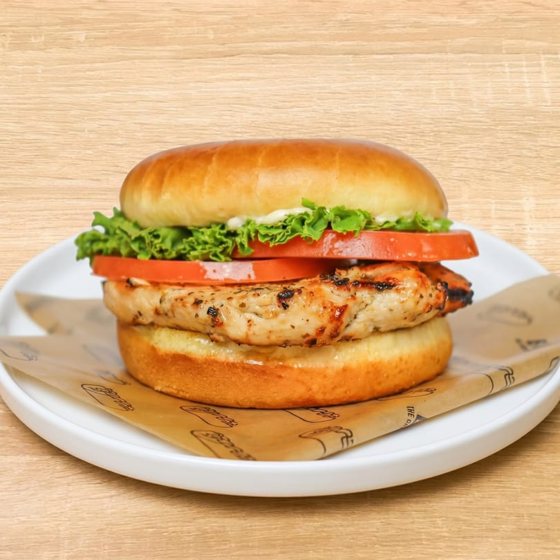 Grilled chicken sandwich with lettuce, tomato, and mayonnaise on a brioche bun, served on a white plate.