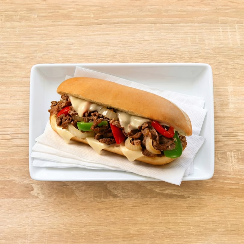 Cheesesteak sandwich with steak, melted cheese, onions, red and green peppers on a white plate.